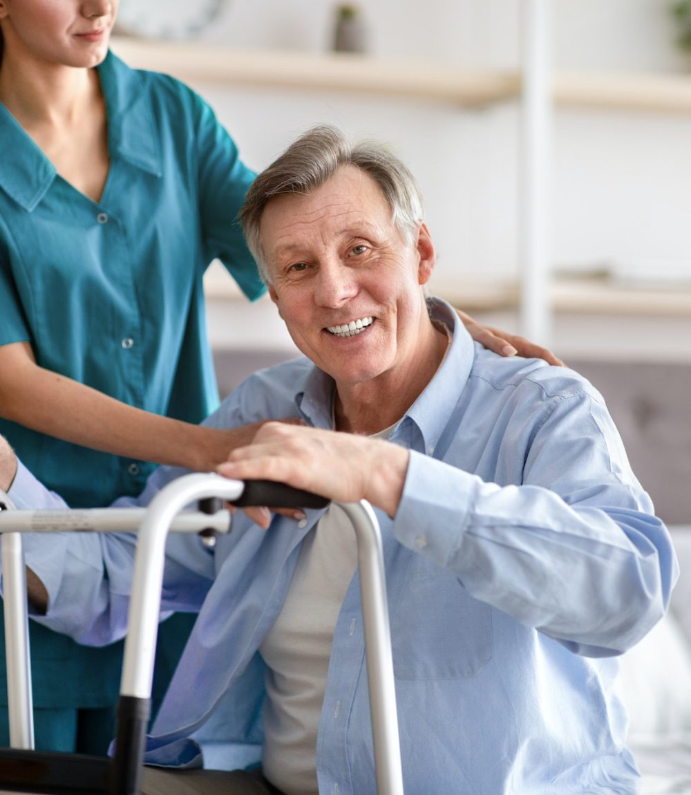 Disabled senior man receiving medical assistance from young caregiver at home, copy space